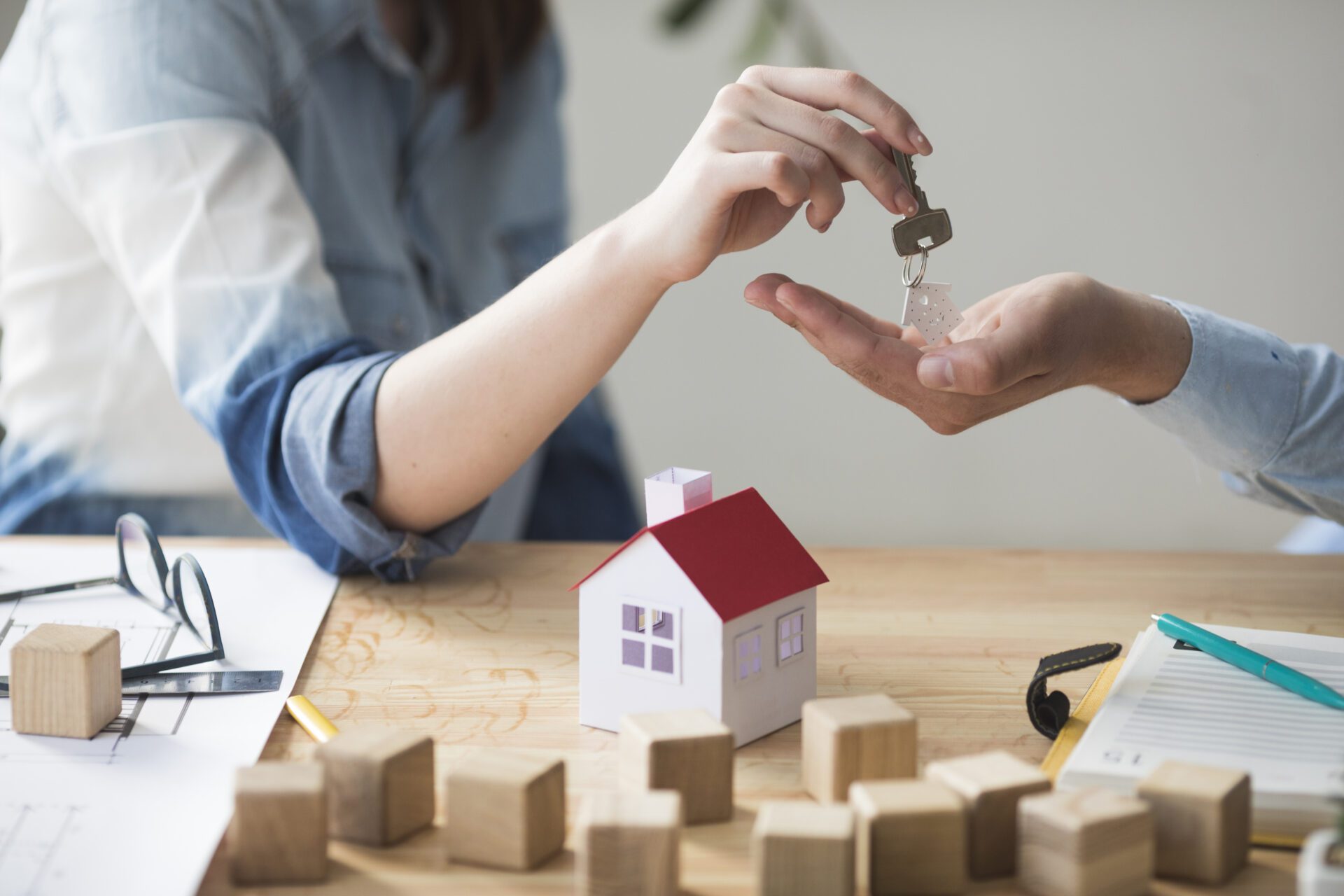 close-up-woman-s-hand-giving-house-key-man-wooden-table Side view hands of agent and client shaking hands after signed contract buy new apartment.